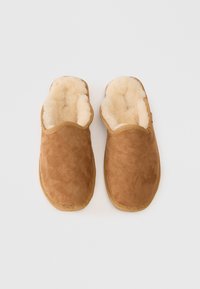 Rjave nubuk copate s mehkob krem notranjosti, zasnova za enostavno obuvanje, zaobljen prst in teksturiran podplat. Brez vidnih dodatkov ali vzorcev.