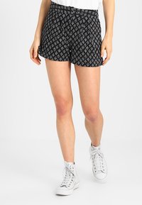 Černobílé šortky s vzorem a volným střihem, zdobené diamantovým designem, sklady a bočními kapsami. V kombinaci s bílými vysokými teniskami.