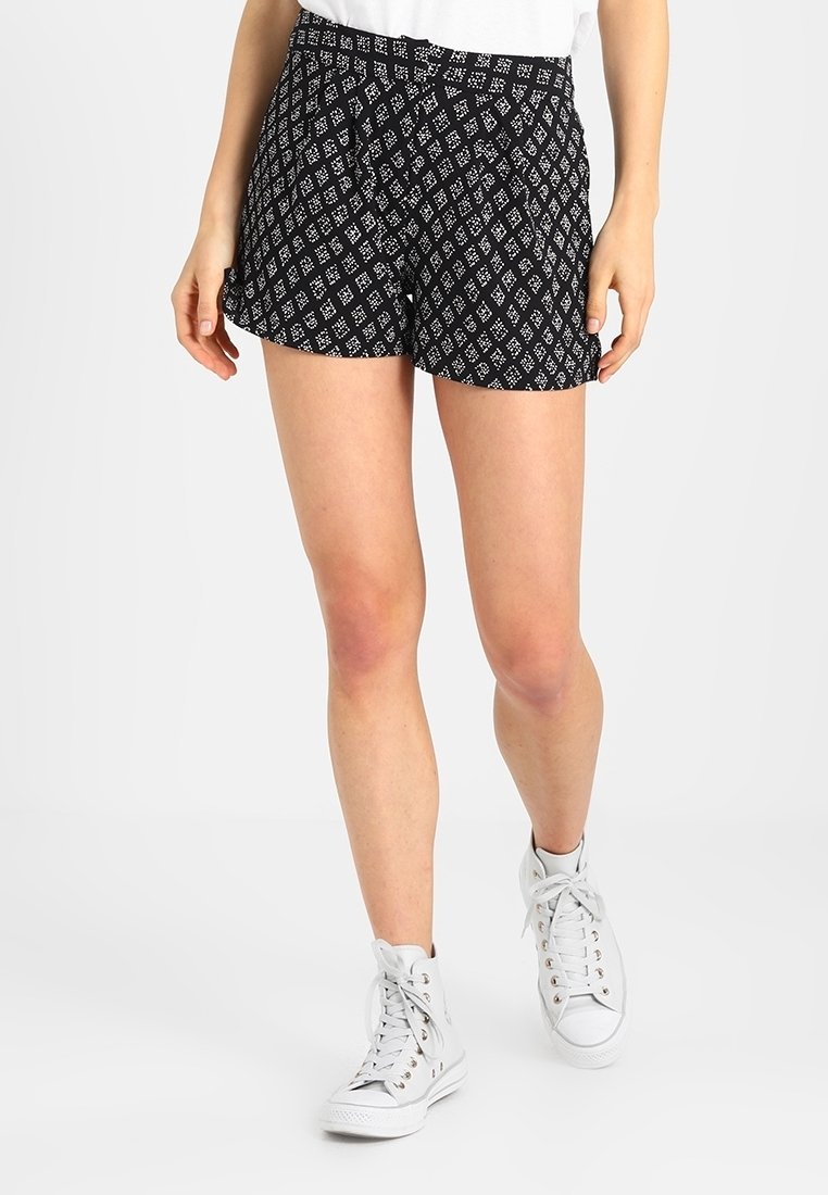 Černobílé šortky s vzorem a volným střihem, zdobené diamantovým designem, sklady a bočními kapsami. V kombinaci s bílými vysokými teniskami.