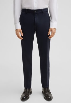 Hosen in Marineblau aus glattem Stoff, mit schlanker Passform, seitlichen Taschen und Knopfverschluss, kombiniert mit braunen Lederschuhen.