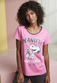 Pink short-sleeve t-shirt featuring a Snoopy graphic with "PEANUTS LAUGH LEAGUE" text, rounded neckline, and relaxed fit.