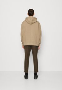 Beżowa bluza z kapturem o luźnym kroju, z przeszyciami i ściągaczem u dołu. Noszona z ciemnooliwkowymi, zwężanymi spodniami oraz czarnymi butami sportowymi.