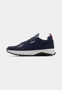Baskets de sport bleu foncé et noir avec semelle blanche, design à lacets, languette rouge au talon et logo "HUGO" sur le côté.