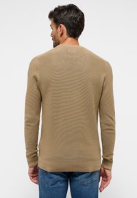 Beige pikkade varrukatega kudumipullover, millel on ümmargune kaelus, horisontaalne ribakujundus, lõpetatud mansetid ja puhas ääre. Kanda siniste teksadega.