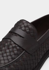 Σκούρο καφέ πλεκτό δερμάτινο μοκασίνι με λείο δερμάτινο λουράκι στο επάνω μέρος, που δείχνει λεπτομερή ραφή και υφή.