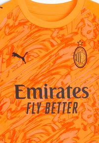 Maglia arancione con un motivo a spirale, logo Puma nero e testo "Emirates Fly Better" sul petto con l'emblema del AC Milan.
