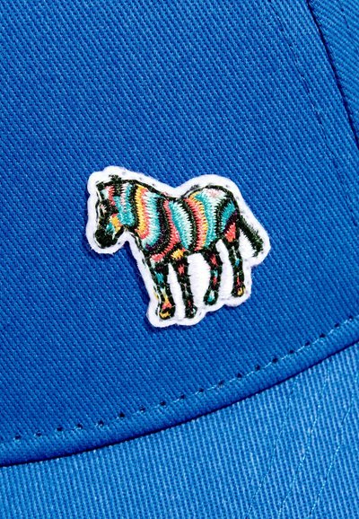 Patch zèbre brodé coloré avec des rayures turquoise, rose, jaune et noires cousues sur un tissu bleu vif, possiblement un vêtement ou un chapeau.