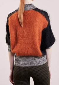Übergroßer Strickpullover in Orange, Schwarz und Grau. Strukturierte Mohairmischung mit geripptem Saum. Raglanärmel und karierte Kragendetails.