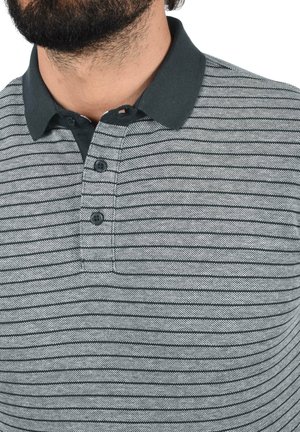 Polo gris et noir à rayures, fabriqué en matière tricotée, avec un col foncé et trois boutons sur le devant. Tissu texturé avec une finition lisse.