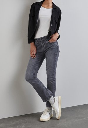 Jeans de mezclilla gris con corte recto, combinados con una camiseta blanca y una chaqueta corta negra. Zapatillas blancas con calcetines grises completan el conjunto.