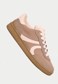 Beige ja valge seemisnahast tossud valgete paeltega ja kummist alusega, nähtavad külgvaates heleda tausta peal.