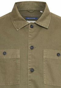 Olive green button-up shirt made of cotton, featuring a collar, two chest pockets, and dark buttons. The texture is smooth with visible stitching.