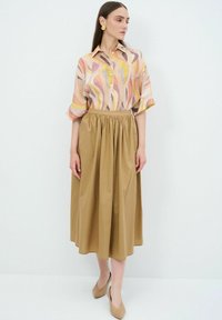Blusa leggera a fantasia nei toni del rosa, arancione e marrone, abbinata a una gonna beige a vita alta e tinta unita. Tessuto morbido, lunghezza al ginocchio.