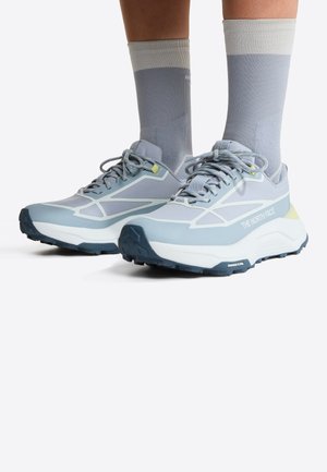 Persoon draagt lichtblauwe en grijze The North Face-sneakers met bijpassende hoge sokken op een witte achtergrond.