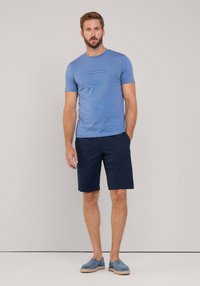 Camiseta azul de manga corta con texto negro, pantalones cortos marinos y zapatos azul claro sin cordones. Diseño sencillo, textura suave y ajuste casual.