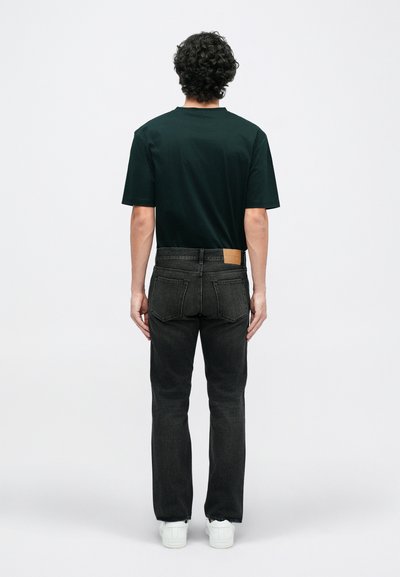 Jeans negri din denim cu croială dreaptă și cusături vizibile, asortați cu un tricou verde închis și adidași albi. Design minimalist.