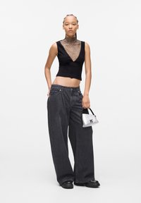 Black sleeveless top with a mesh neckline, wide-leg dark denim jeans, and a silver handbag. Model wears black platform shoes.