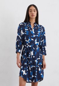 Abito blu navy con un audace motivo astratto bianco e azzurro, dotato di un colletto, vita avvolta da una cintura e maniche ampie. Tessuto morbido.