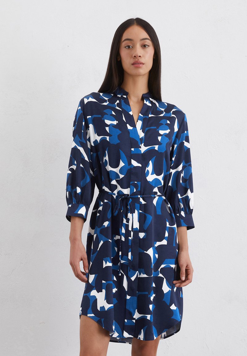 Abito blu navy con un audace motivo astratto bianco e azzurro, dotato di un colletto, vita avvolta da una cintura e maniche ampie. Tessuto morbido.