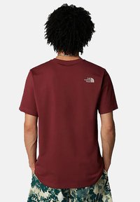 Camiseta de manga corta color marrón, hecha de tela suave, con un pequeño logo blanco en la parte posterior superior y un corte holgado.