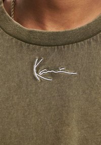 Olive green sweatshirt with a ribbed neckline and white embroidered logo on the front. Soft texture, casual design, and minimal detailing.