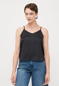 Svart satin cami med V-hals, tynne justerbare stropper og en avslappet passform, satt sammen med høye denimjeans.