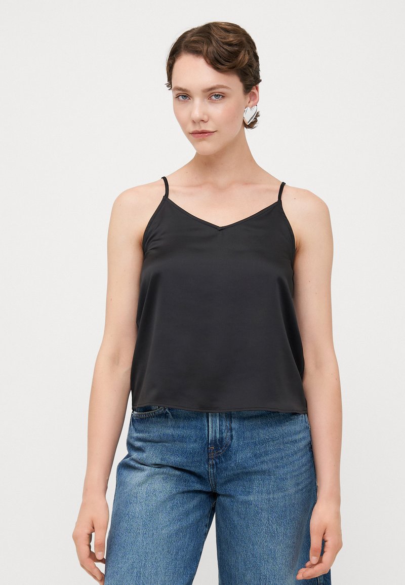 Svart satin cami med V-hals, tynne justerbare stropper og en avslappet passform, satt sammen med høye denimjeans.