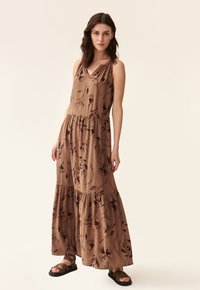 Maxime dress in ruskea kangas, jossa on kukkakuosi, hihaton muotoilu, v-pääntie ja kerrostettu helma. Yhdistetty mustiin sandaaleihin.