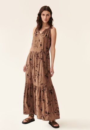 Maxi dress in brown fabric featuring a floral print, sleeveless design, v-neck, and tiered hem. Paired with black sandals.
