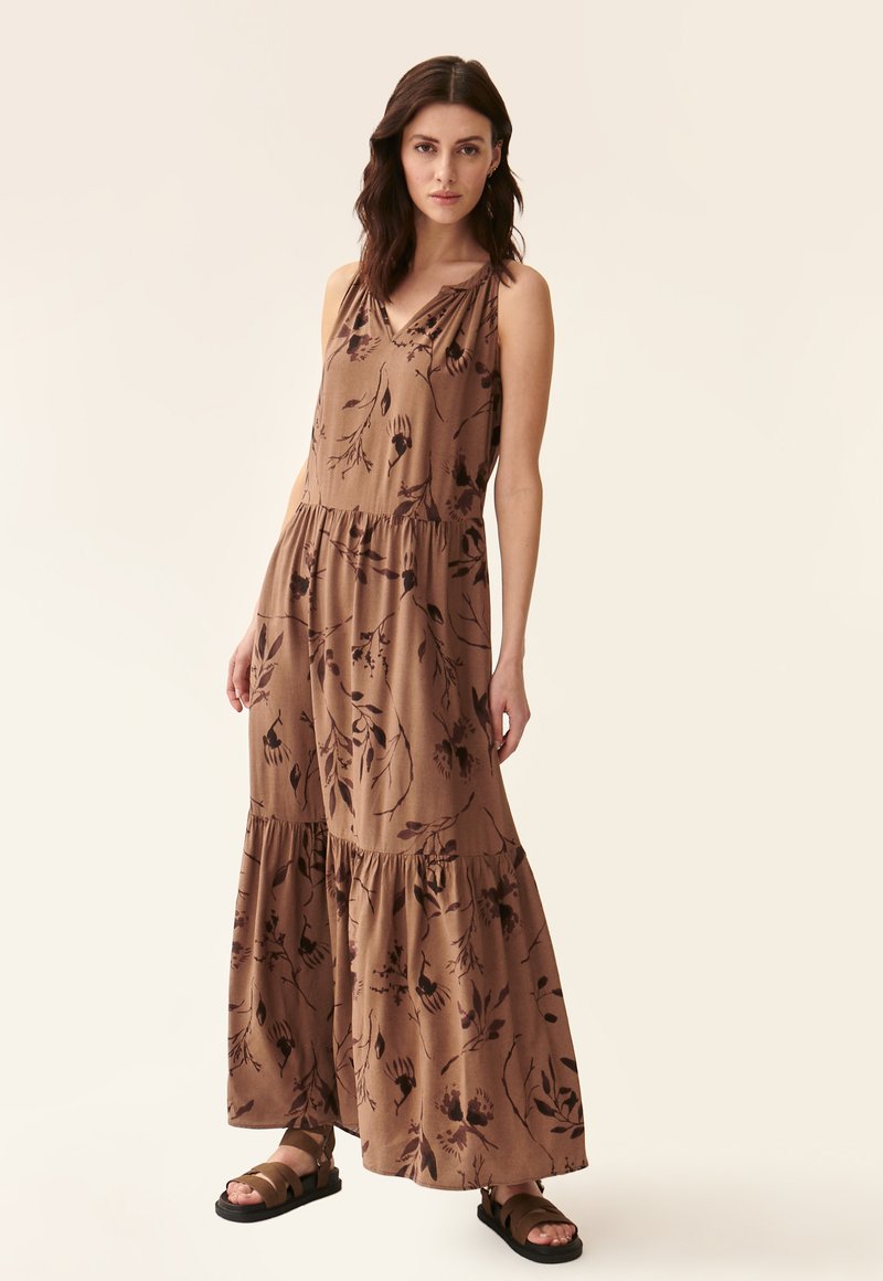 Maxime dress in ruskea kangas, jossa on kukkakuosi, hihaton muotoilu, v-pääntie ja kerrostettu helma. Yhdistetty mustiin sandaaleihin.