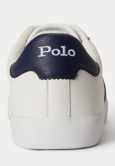 Λευκός τακούνι αθλητικού παπουτσιού με υφή στη σόλα και μπλε δερμάτινο σημείο κεντημένο με τη λέξη "Polo" σε λευκή κλωστή.