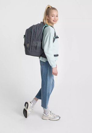Zaino grigio con dettagli turchesi, spallacci regolabili e molteplici tasche. Indossato con una felpa blu chiaro e jeans blu strappati.