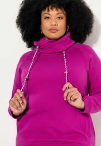 Sudadera fucsia con cuello alto, cuenta con cordones blancos y rosas y detalles dorados. La tela suave y los puños acanalados añaden textura.