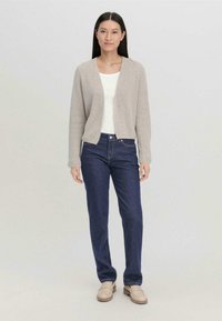 Lichtgrijze gebreide cardigan met een relaxte pasvorm, gedragen over een witte top, gecombineerd met donkerblauwe jeans en beige instappers. Eenvoudig ontwerp.