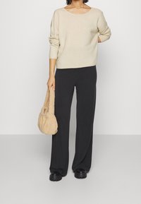 Lichtbeige, gebreide trui met een wijde halslijn; gecombineerd met zwarte, losse broek en een fuzzy beige handtas. Zwarte, chunky schoenen.