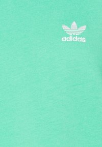 Mint green cotton fabric featuring a small white embroidered Adidas logo with a trefoil design positioned on the left side.