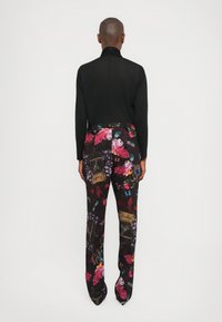 Zwarte langemouwtop met hoge hals; bloemenpatroon broek met rood, roze en gouden accenten; zachte texturen, aansluitende silhouet.