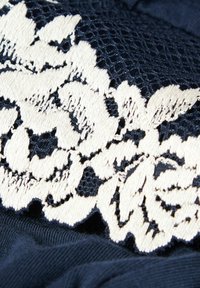 Marine stof met een witte bloemenkant overlay, met complexe borduursels en open kantsecties die contrast bieden in textuur en ontwerp.