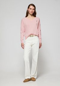 Ljust rosa v-ringad tröja, vita vida byxor, bruna loafers. Tröjan har en liten emblem på vänster bröst, mjuk textur, avslappnad passform.