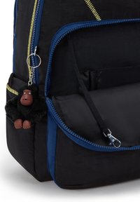 Zaino nero con dettagli blu, dotato di chiusura a zip e un portachiavi a forma di gorilla nero. Diverse tasche per riporre oggetti.