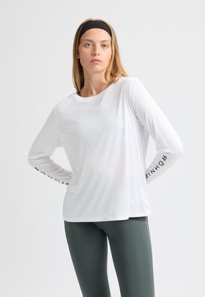 Maglietta atletica bianca a maniche lunghe con scollatura rotonda e lettere nere sulle maniche, abbinata a leggings verde scuro.