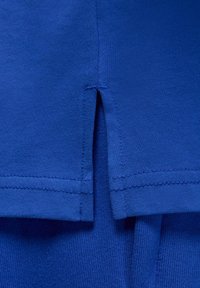 T-shirt in cotone blu con design a orlo spaccato, texture morbida e dettagli di cucitura a contrasto nelle cuciture.