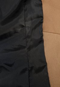 Gros plan de tissu noir et marron montrant une surface texturée avec une finition brillante sur le côté noir et un aspect mat sur le côté marron, séparés par une couture.