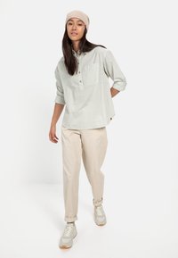 Lysegrønt og hvidt stribet skjorte med lange ærmer, parret med beige bukser og lyse sneakers. Modellen bærer en beige hue.