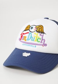 Fehér és tengerészkék sapka, amelyen a "Von Dutch" hímezett logó található egy karton szemmel és szárnyakkal, strukturált kialakítással és texturált napellenzővel.