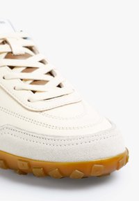 Baskets couleur crème avec une tige en cuir lisse, des accents en daim, des lacets ronds et une semelle en caoutchouc texturée avec des reliefs.