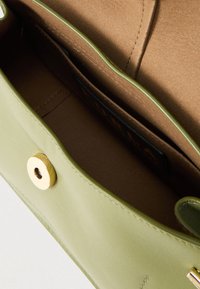 Φωτεινή πράσινη δερμάτινη τσάντα χειρός με ανοικτό πάνω μέρος που αποκαλύπτει καφέ σουέντ εσωτερικό και μαγνητικό χρυσό κουμπί κλεισίματος.