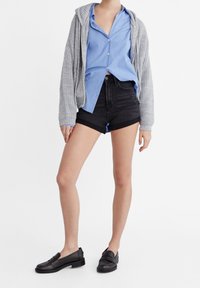 Un hoodie gris en tricot superposé sur une chemise à rayures bleues à boutons, associé à un short en denim noir et des mocassins noirs. Tenue simple et décontractée.