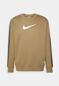 Brun bomullströja med en vit Nike-logotyp på bröstet och svarta sidosidostripes med upprepad text. Rund halsringning och långa ärmar.