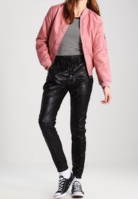 Rosa Bomberjacke, gestreiftes Shirt, schwarze Kunstlederhosen und schwarze Sneakers mit weißen Sohlen. Lässiges urbanes Outfit mit elastischen Bündchen.